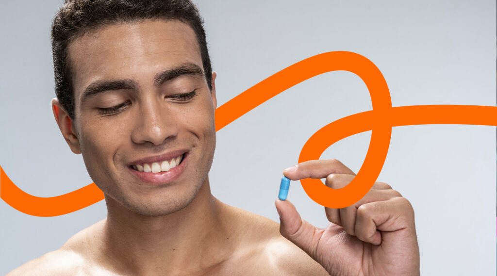 Smiling man holds a blue capsule between his fingers against a light gray background with an orange decorative loop behind him.