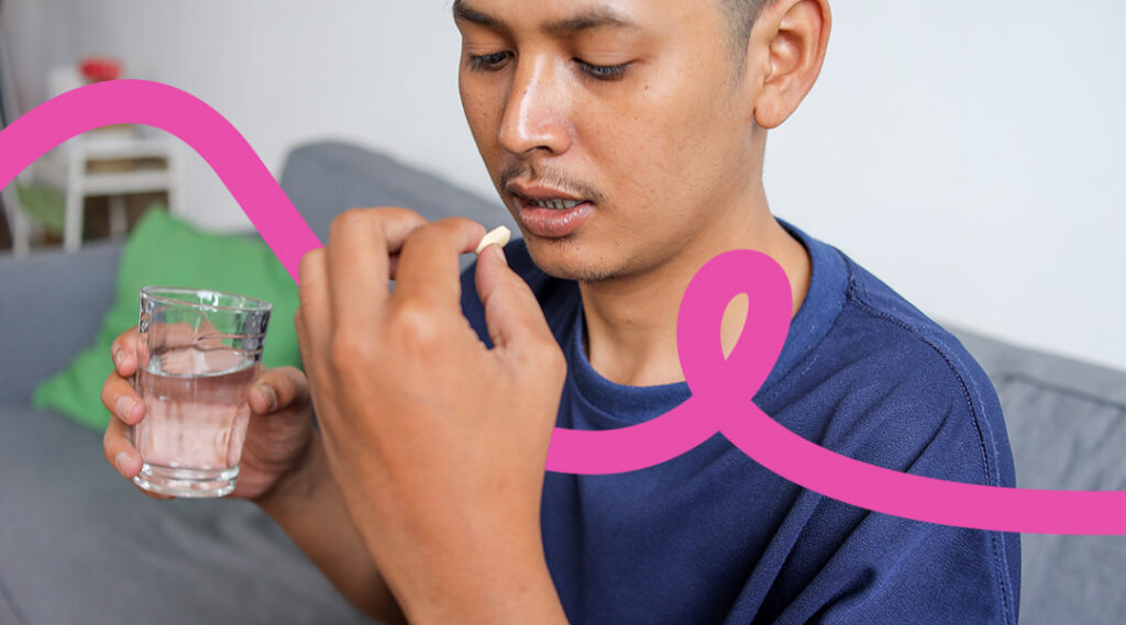 Man sitting on a couch holding a pill near his mouth and a glass of water, ready to take it.